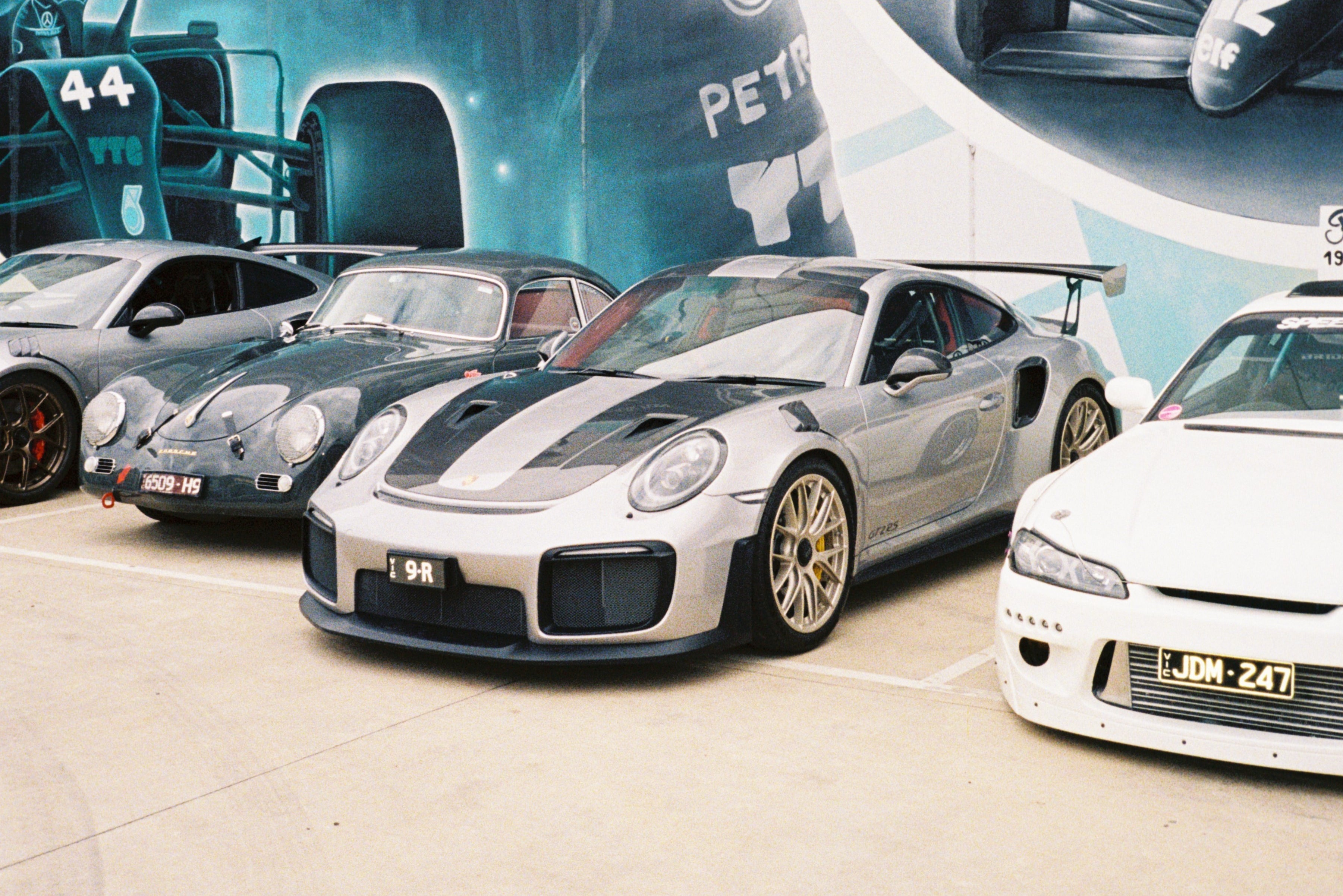 Supercars and Japanese cars parked in-front of a Lewis Hamilton mural