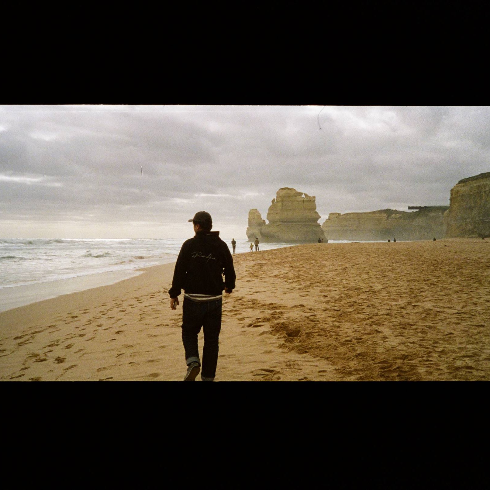 Person walking on a beach with cliffs and ocean under a cloudy sky