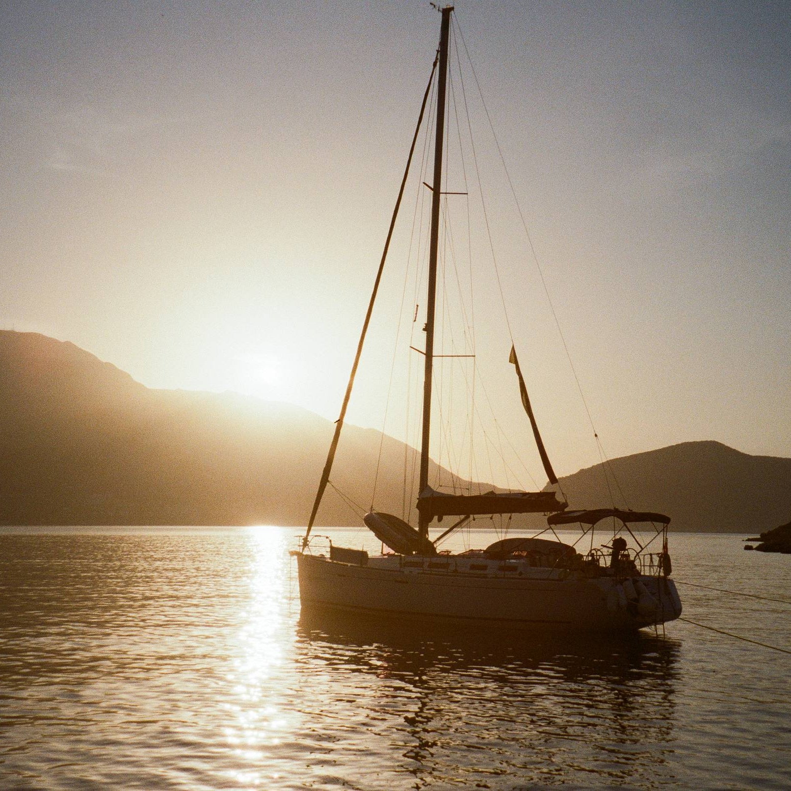 Sailboat on a calm lake with mountains in the background during sunset.