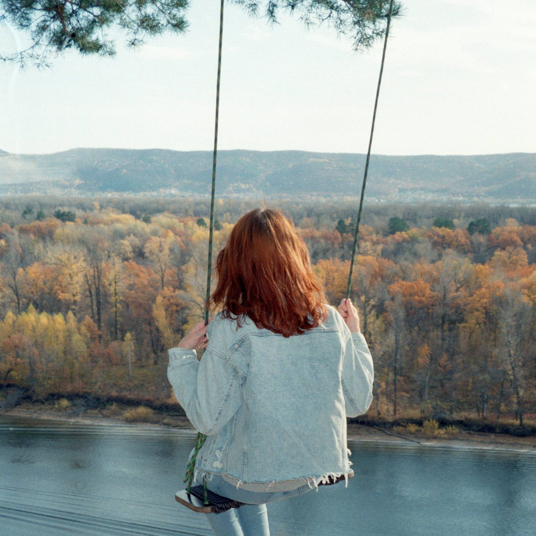 Person swinging on a rope swing over a body of water with autumn trees in the background