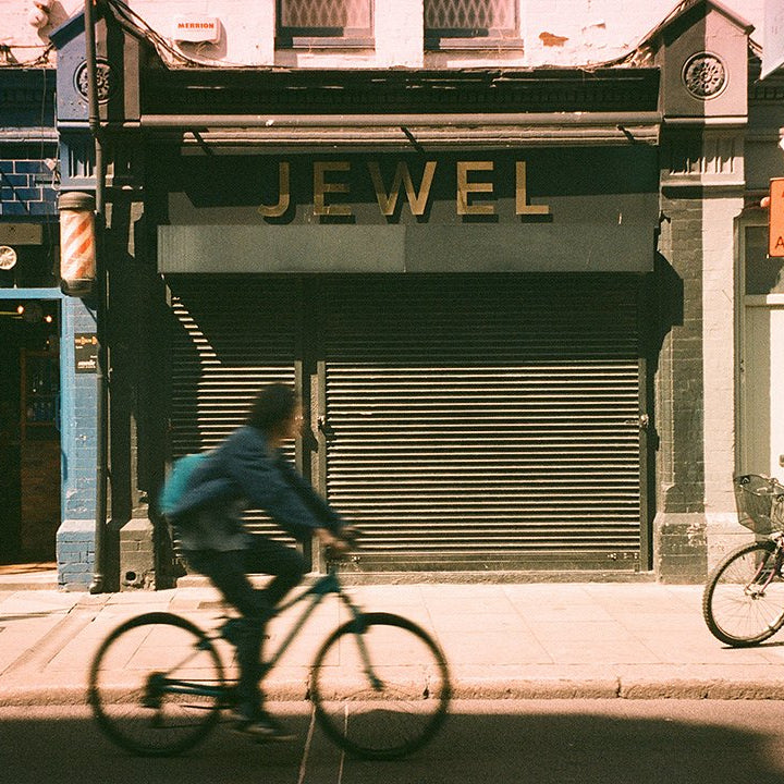 Man riding a bicycle past a closed jewelry store with 'Jewel' displayed on the shutter.