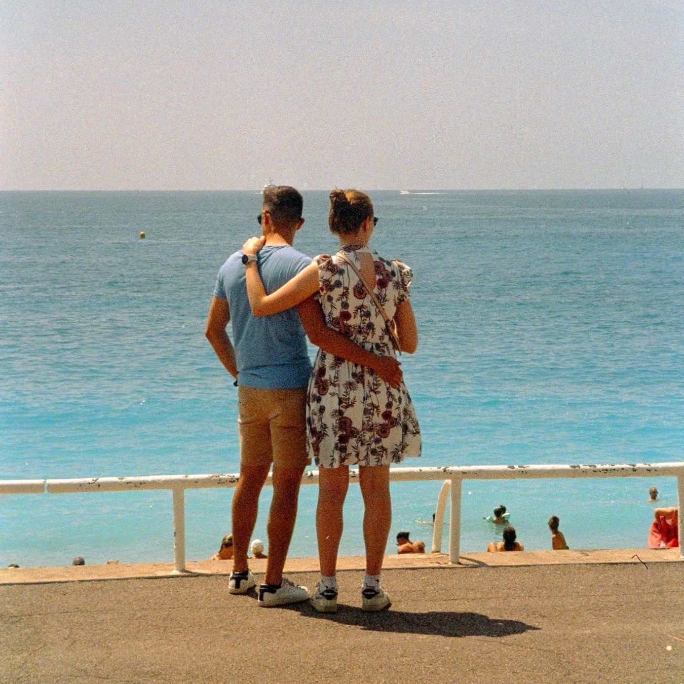 Two people standing on a promenade by the sea, looking out at the water.