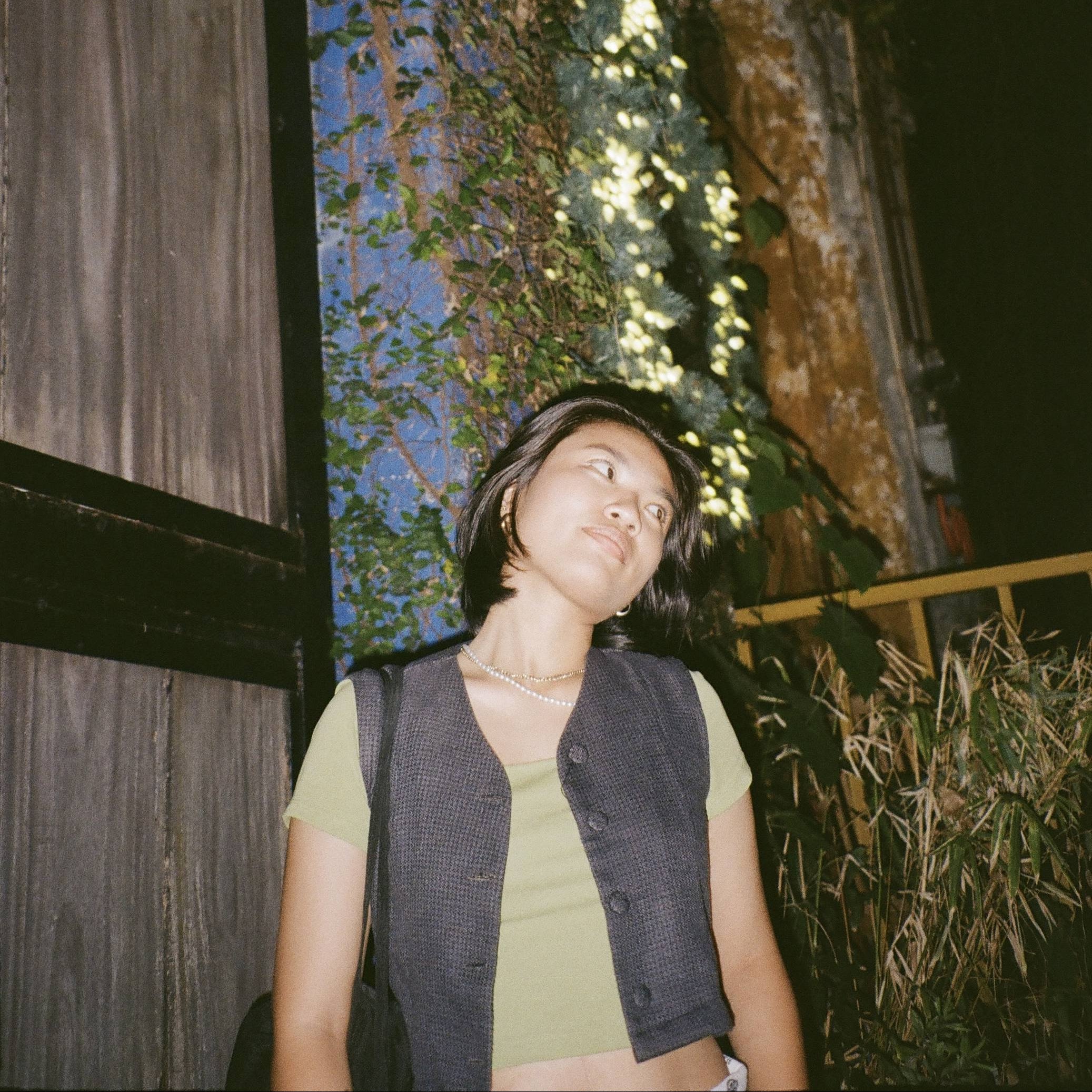 Person standing outdoors with a building and neon sign in the background