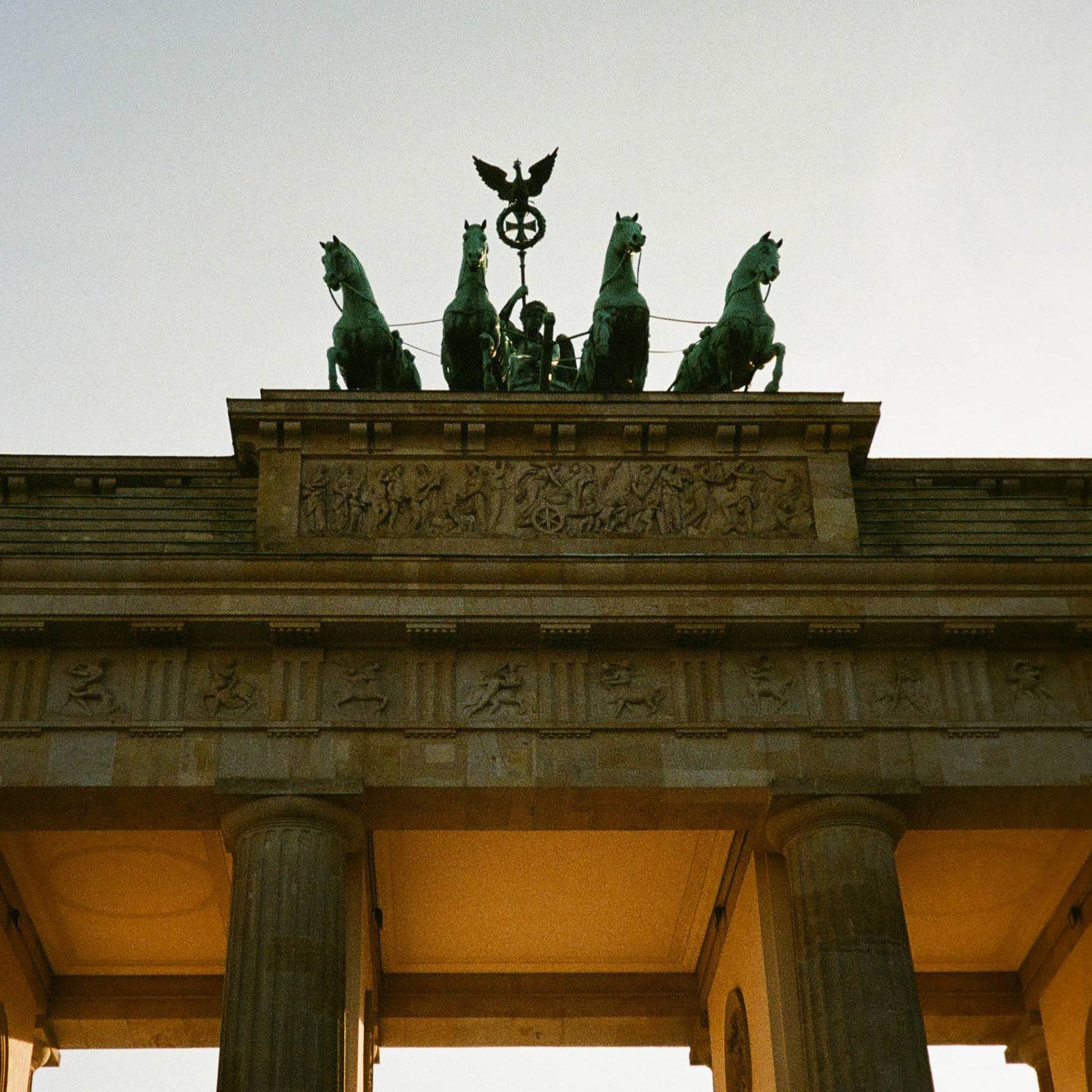 Top of the Brandenburg Gate with statues and an eagle emblem against a clear sky.
