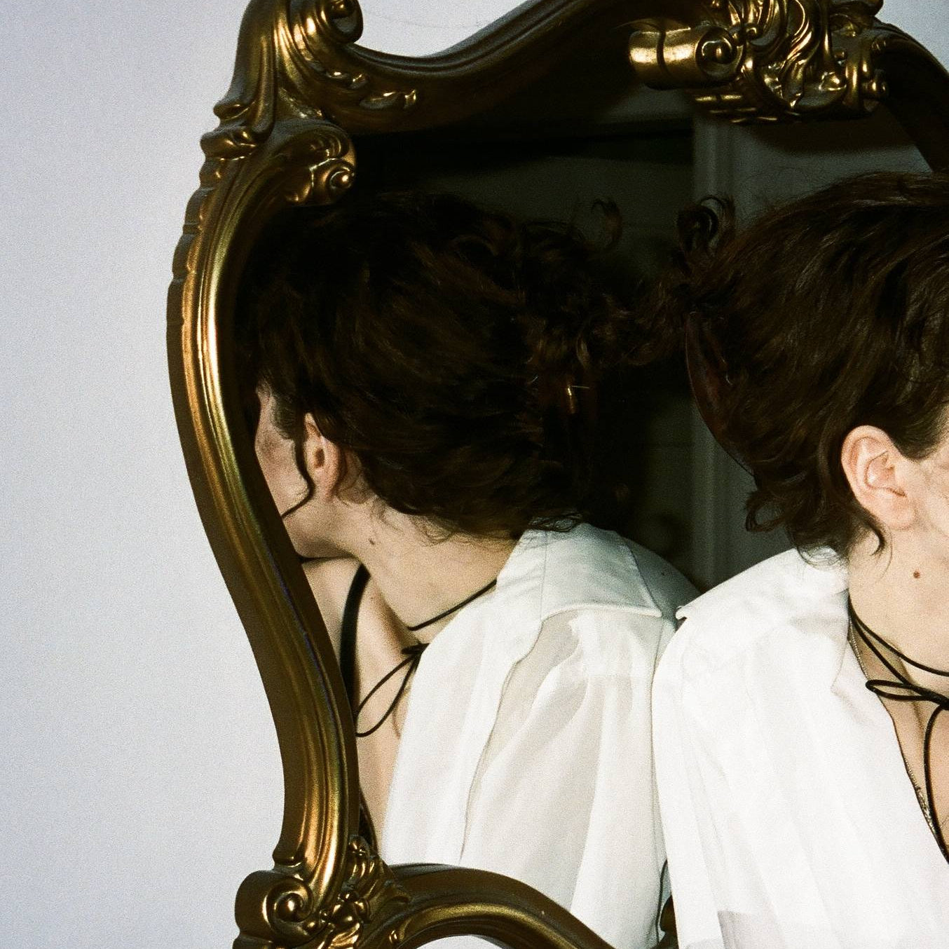 Person looking away from a decorative gold-framed mirror.