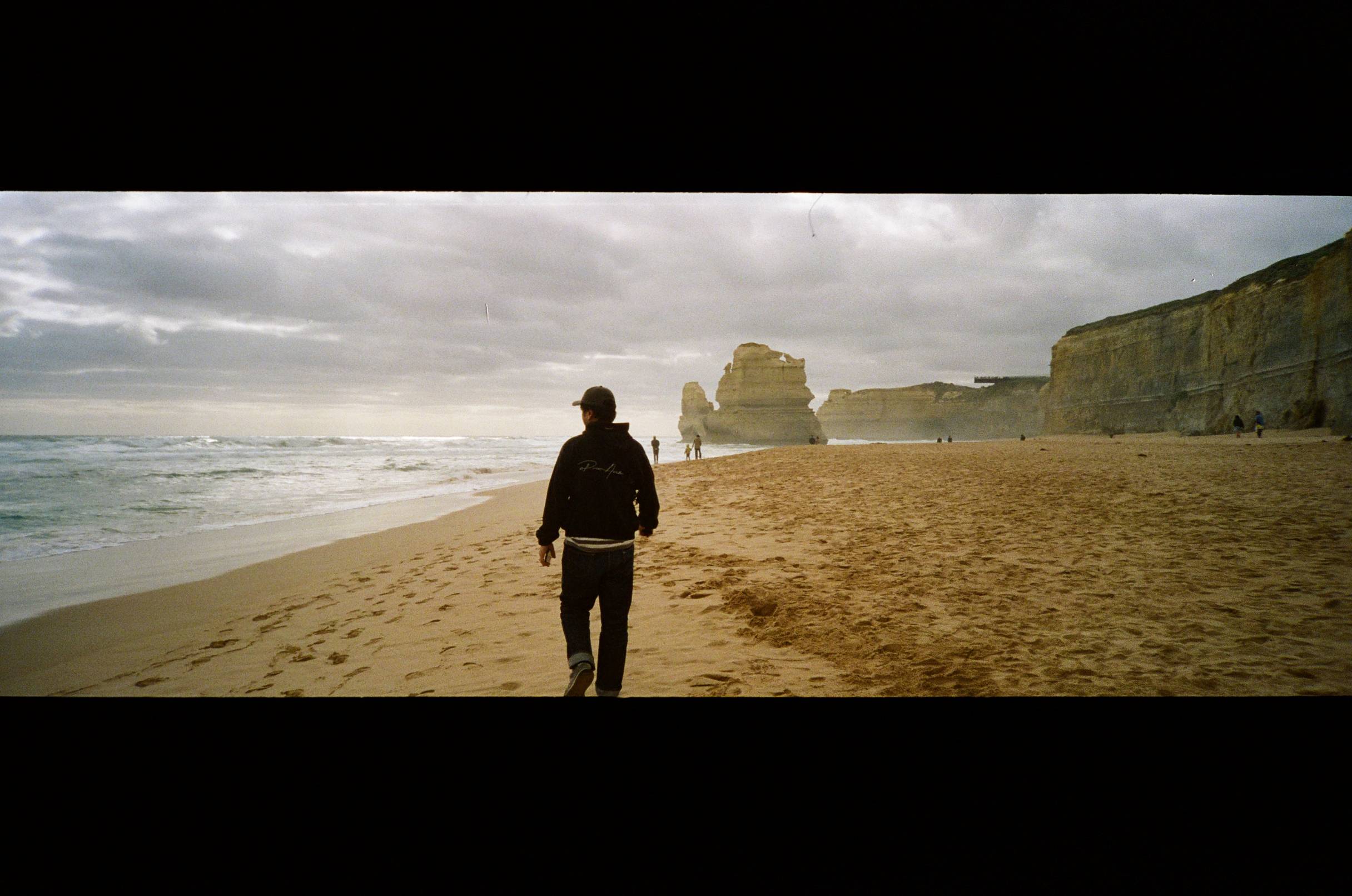 Person walking on a beach with cliffs and ocean under a cloudy sky