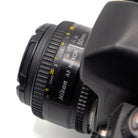 Close-up of a Nikon AF Nikkor 50mm f/1.8D lens attached to a camera body, showing the focus ring, distance scale, and Nikon branding on a white background.