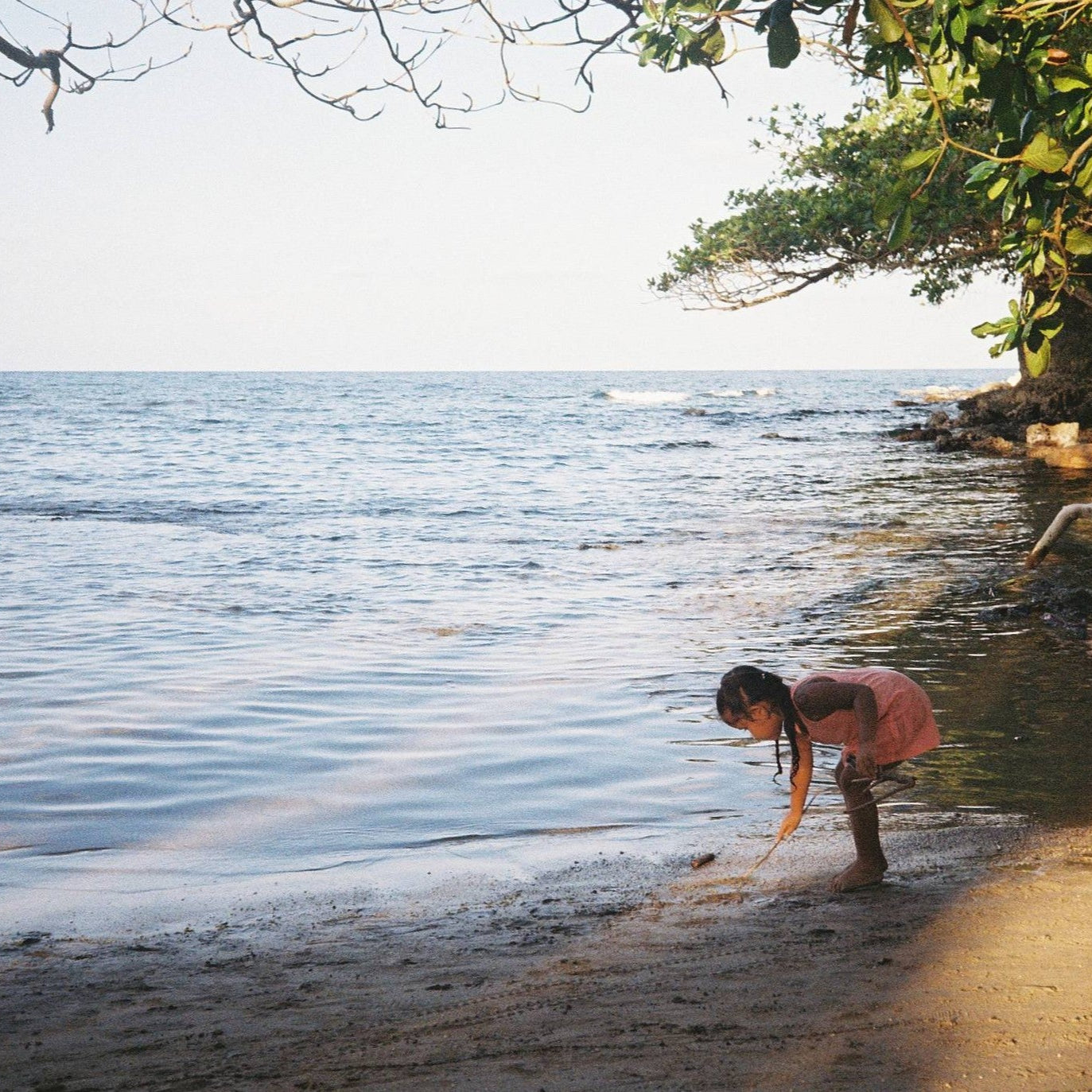 Child playing by the water's edge with trees and foliage in the background