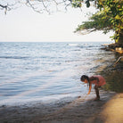 Child playing by the water's edge with trees and foliage in the background