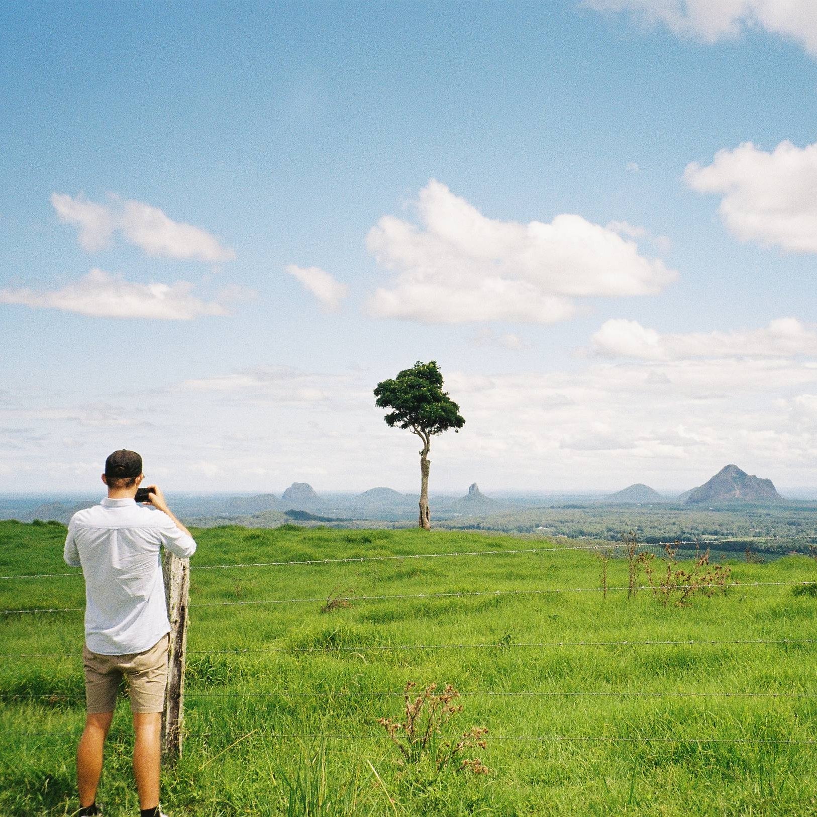 Man taking a photo of a scenic landscape with mountains and a clear sky.