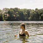 Person in a black swimsuit standing in a lake with trees in the background