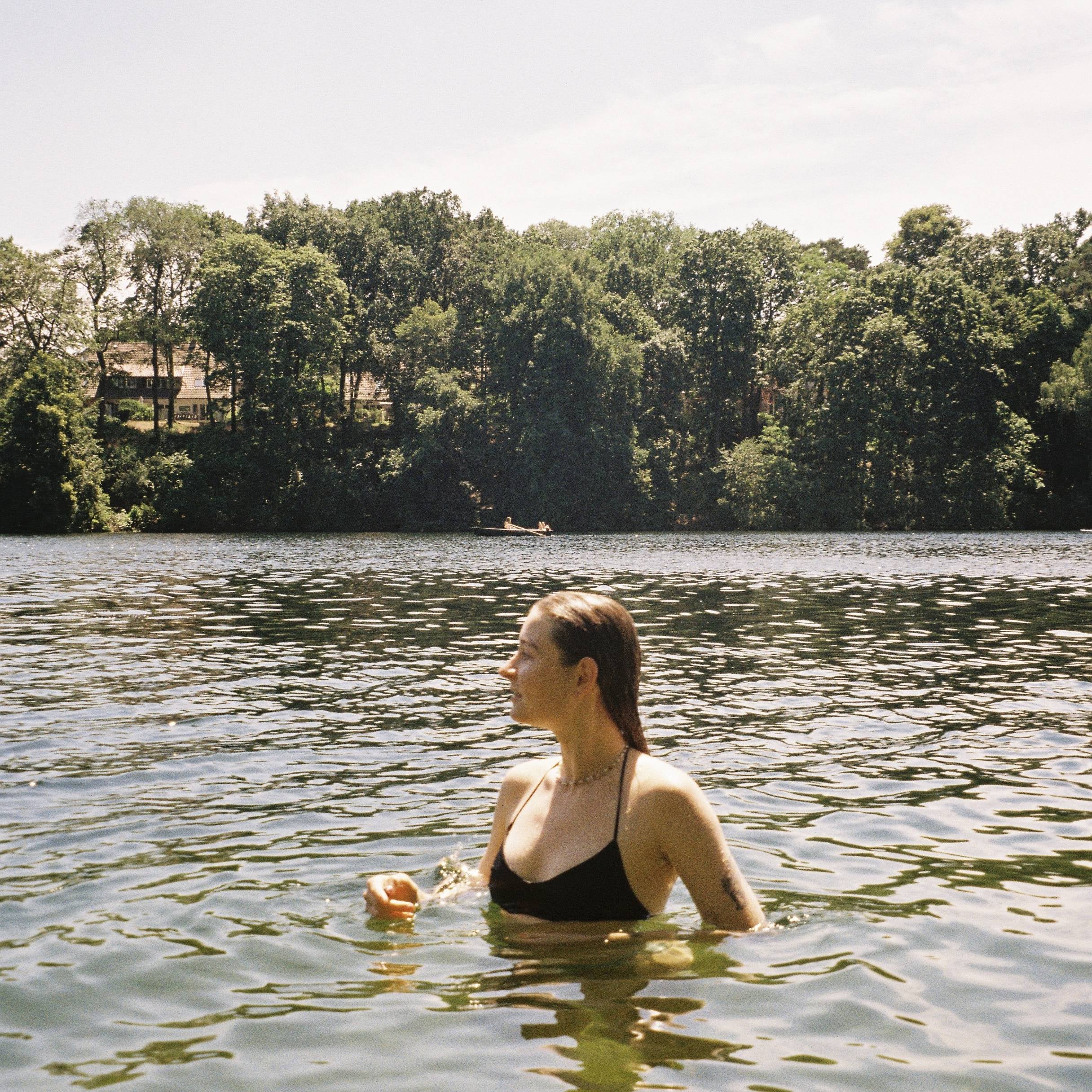 Person in a black swimsuit standing in a lake with trees in the background